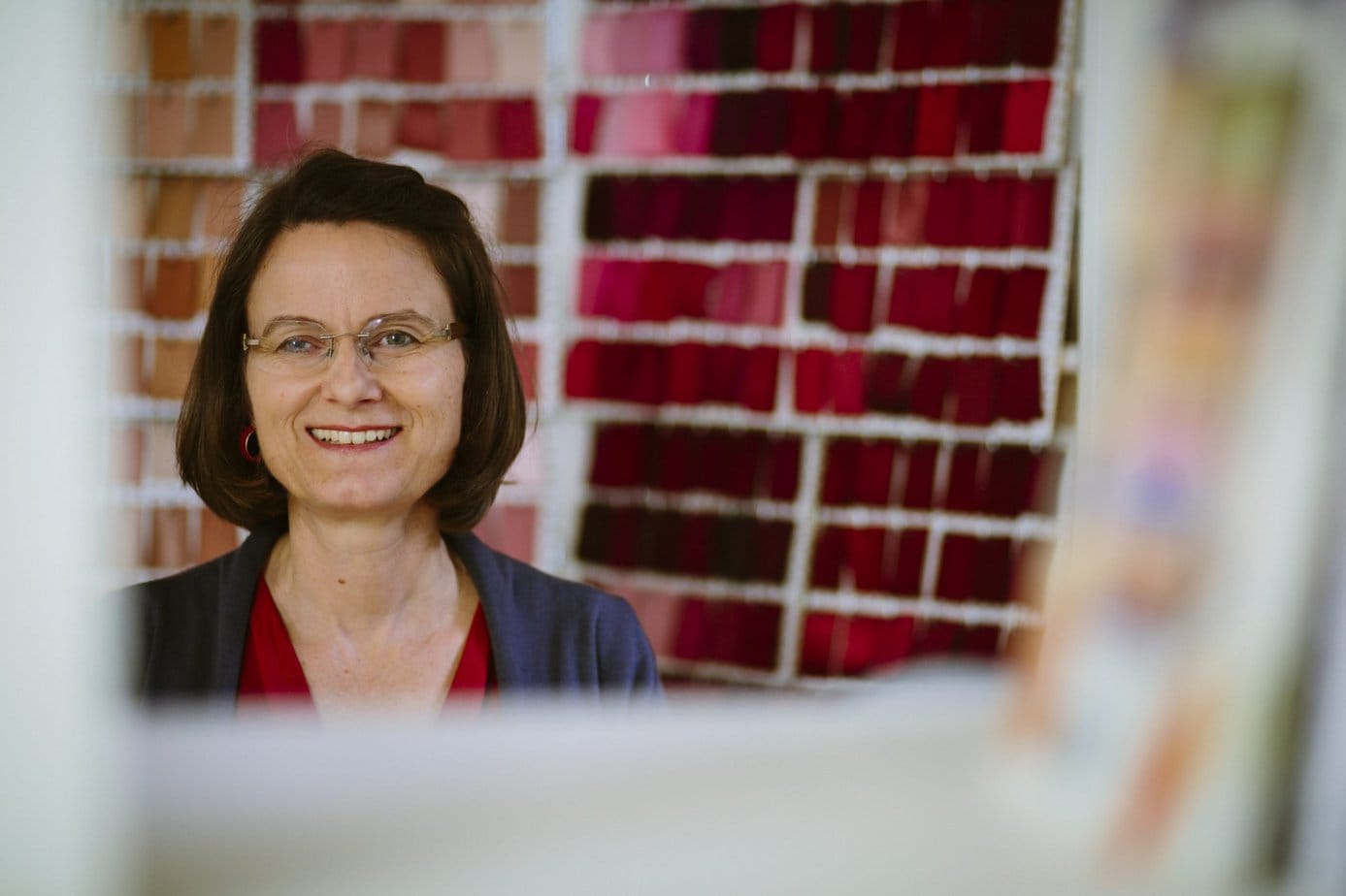 Stefanie Sauer-Bloch steht in ihrem Atelier vor einem Teil ihrer Farbenwand mit Stoffen für die Farbberatung, hier sind es die Rottöne.