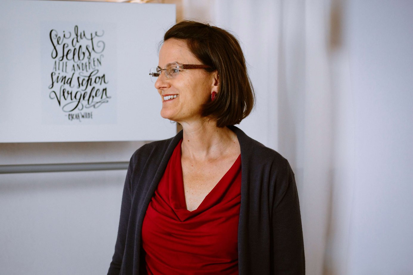 Foto von Stefanie Sauer-Bloch, sie steht vor einem Schrank auf dem der Spruch von Oscar Wilde steht: Sei du selbst, alle anderen gibt es schon.